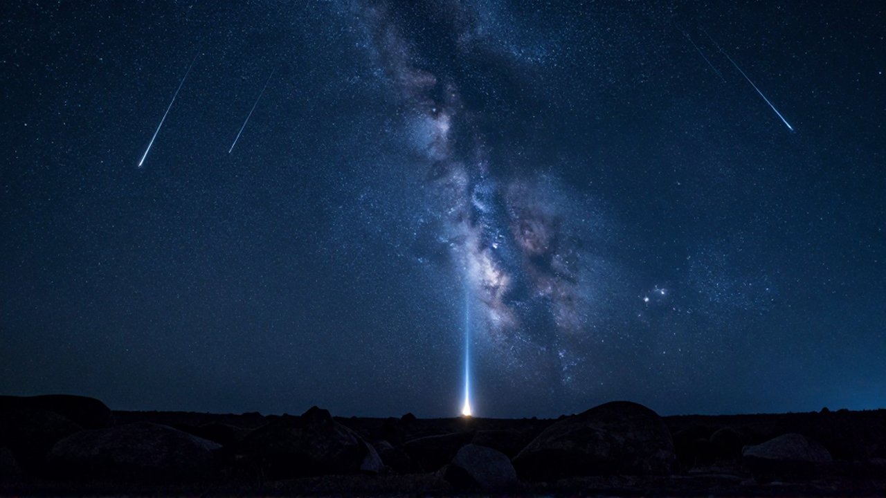 Lluvia de meteoros cruzando un cielo nocturno estrellado sobre un paisaje rocoso oscuro.