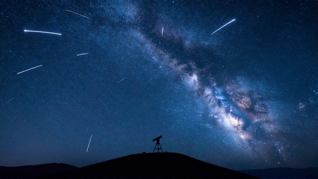Lluvia de meteoros brillantes surcando un cielo estrellado con la silueta de un telescopio en una montaña.